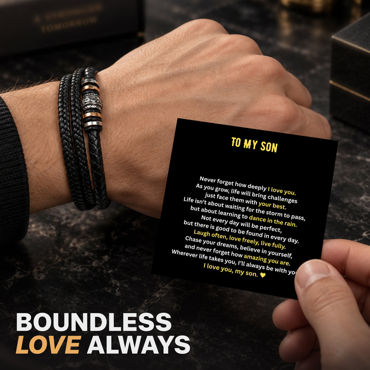 Hand holding a To My Son message card above a braided black leather bracelet on a black gift box